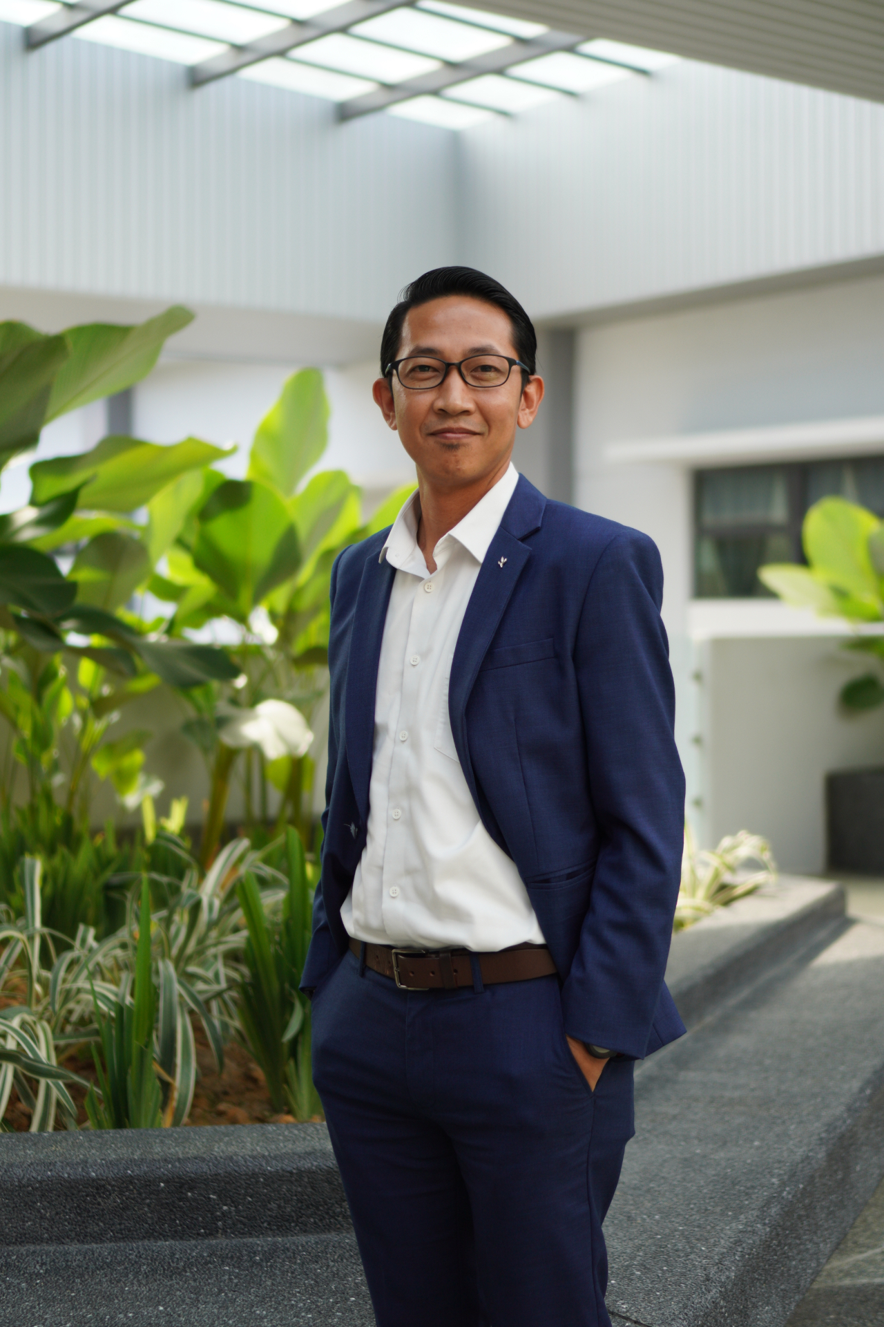 Dr Fitri Zainuddin, Consultant Psychiatrist, wearing a dark suit and tie, smiling warmly at the camera against a soft neutral backdrop.